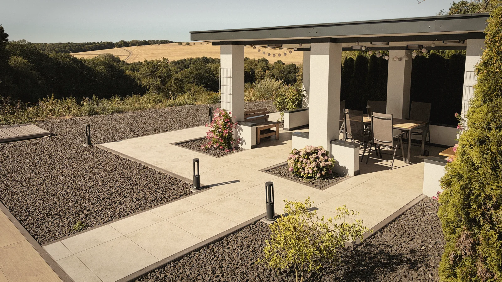 Überdachte Terrasse mit langem Tisch, dahinter offene Felder
